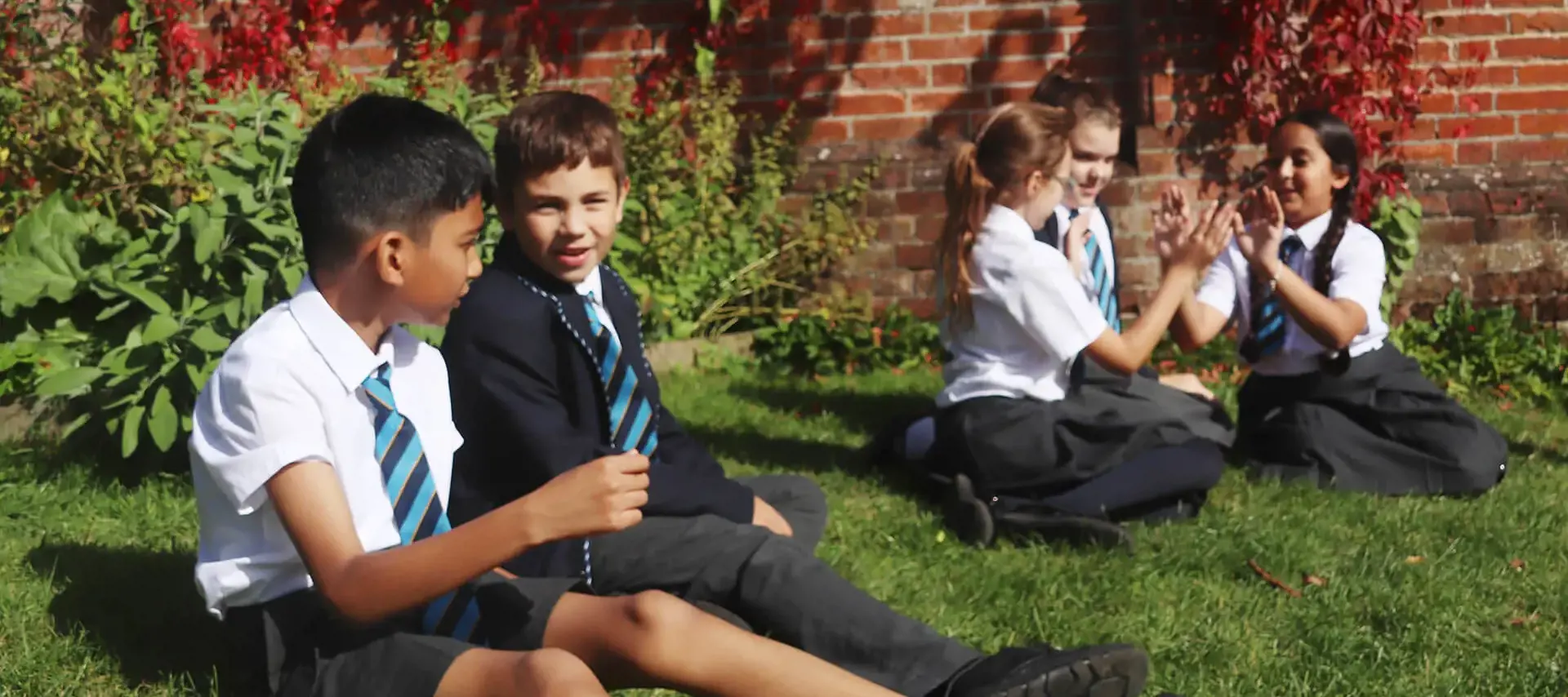 Prep School pupils sitting on grass in the School grounds at The Gregg Prep, a private school in Southampton